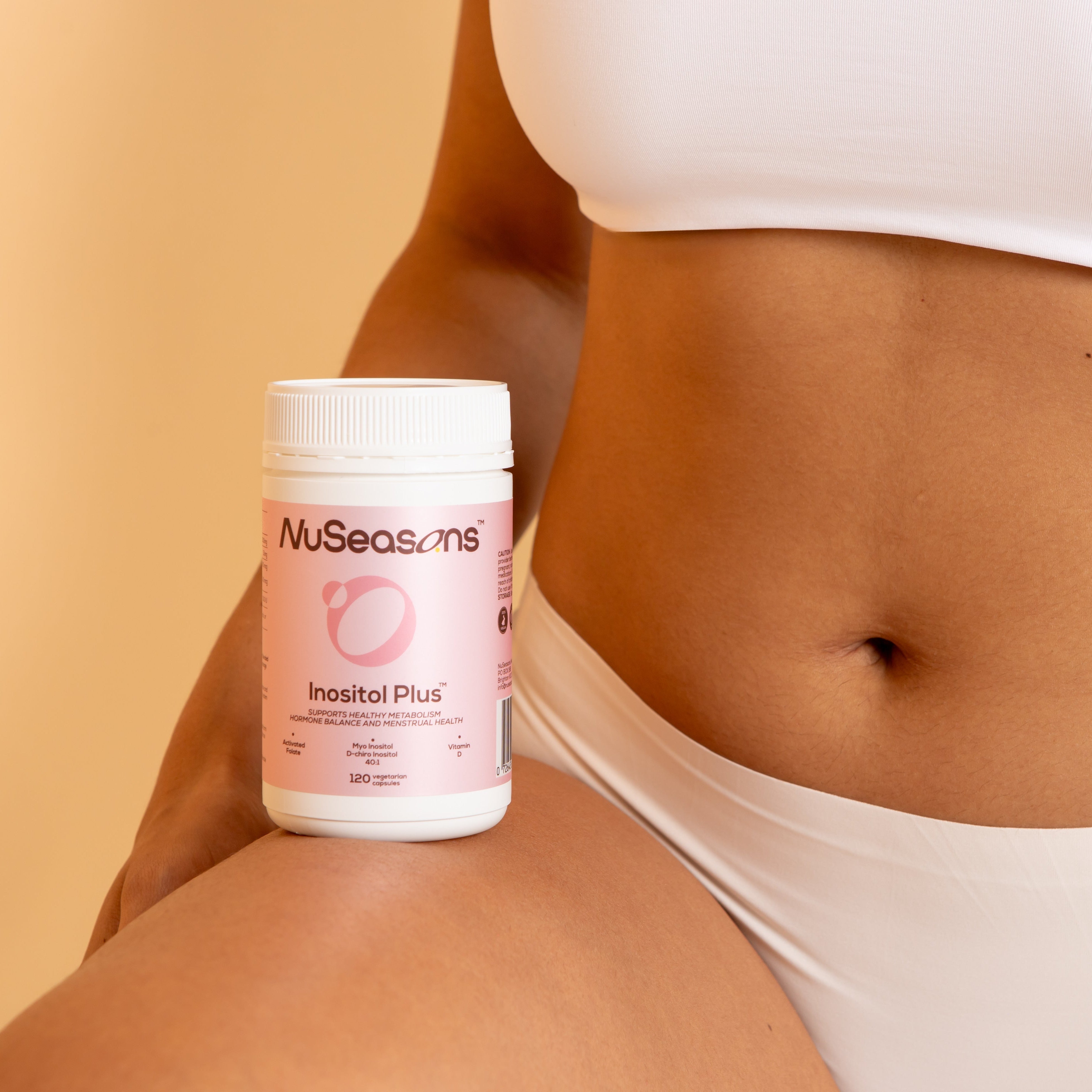 Person holding a bottle of NuSeasons Inositol Plus supplement against a beige background